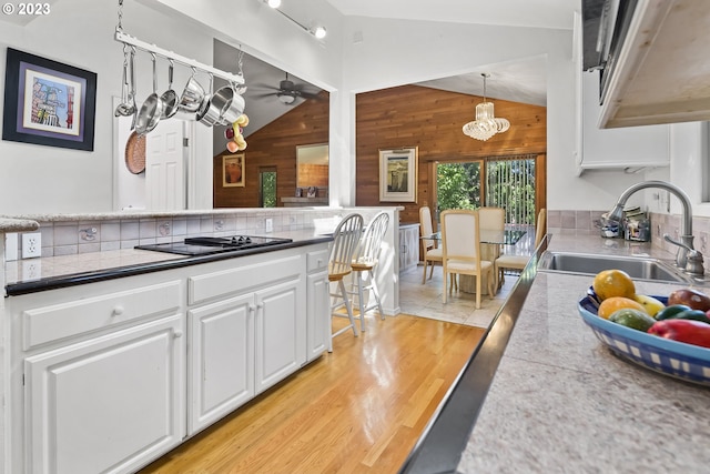 kitchen featuring light hardwood / wood-style floors, ceiling fan with notable chandelier, wooden walls, white cabinetry, and sink