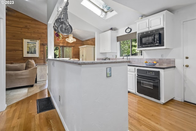 kitchen featuring wood walls, a skylight, light hardwood / wood-style flooring, black appliances, and white cabinets