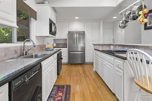 kitchen featuring light wood-type flooring, backsplash, sink, black appliances, and white cabinets