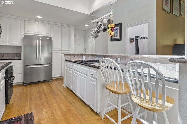 kitchen with white cabinets, tasteful backsplash, stainless steel fridge, and light hardwood / wood-style flooring