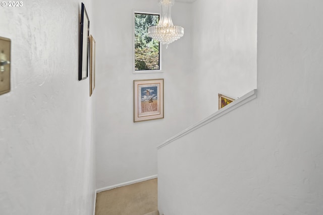 staircase with an inviting chandelier and light colored carpet