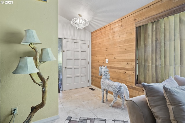 tiled foyer entrance with wooden walls, a notable chandelier, and vaulted ceiling