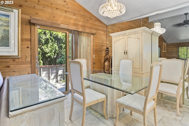 dining space featuring lofted ceiling, ceiling fan with notable chandelier, light tile floors, and wooden walls