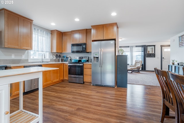 kitchen featuring wood finished floors, stainless steel appliances, light countertops, a sink, and recessed lighting