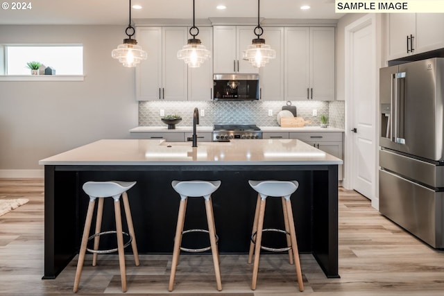 kitchen with backsplash, stainless steel appliances, sink, light wood-type flooring, and a kitchen island with sink