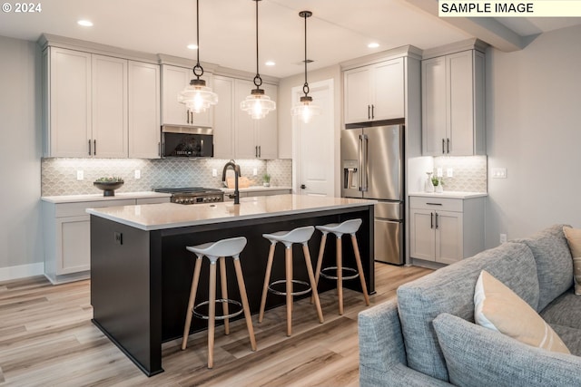 kitchen featuring backsplash, stainless steel appliances, light hardwood / wood-style flooring, a kitchen island with sink, and a breakfast bar area