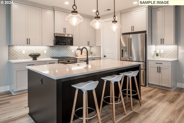 kitchen with stainless steel appliances, a center island with sink, light hardwood / wood-style floors, and tasteful backsplash