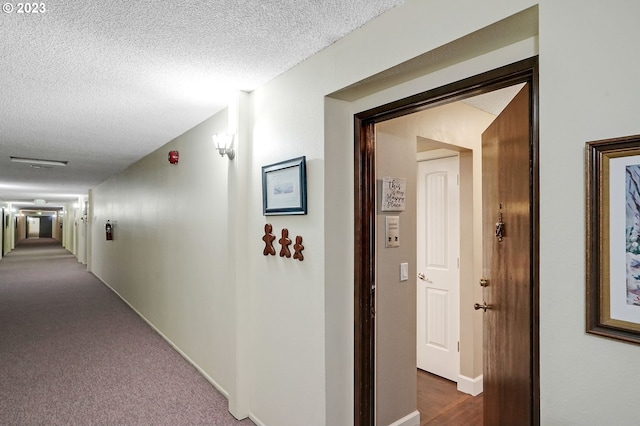 hallway with baseboards, a textured ceiling, and dark carpet