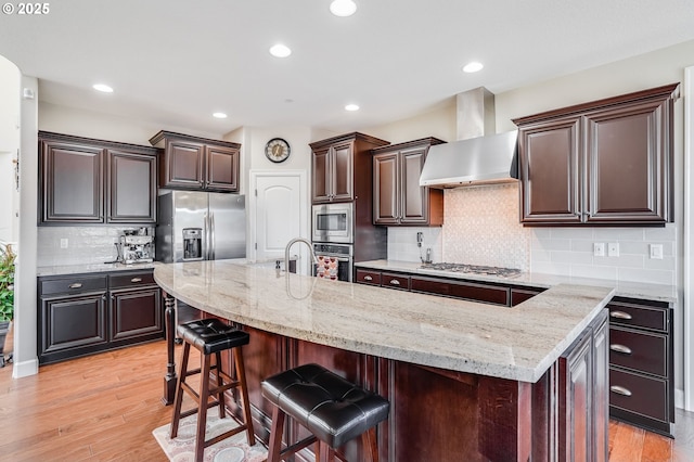 10703 NW Glenmore Way, Portland, OR 97229 - kitchen with wall chimney exhaust hood, stainless steel appliances, light stone counters, a kitchen bar, and a center island with sink