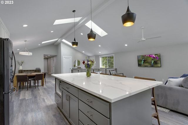 kitchen featuring light wood-type flooring, stainless steel refrigerator, ceiling fan, vaulted ceiling with skylight, and light stone countertops