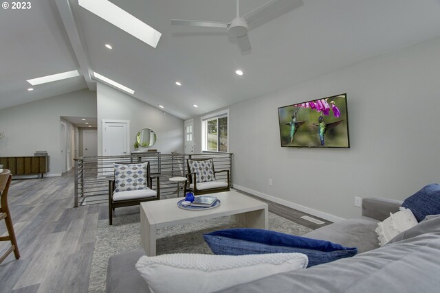 living room featuring lofted ceiling with skylight, ceiling fan, and light wood-type flooring