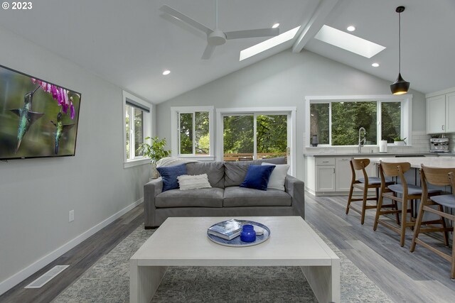 living room featuring light hardwood / wood-style floors, a skylight, ceiling fan, sink, and beam ceiling