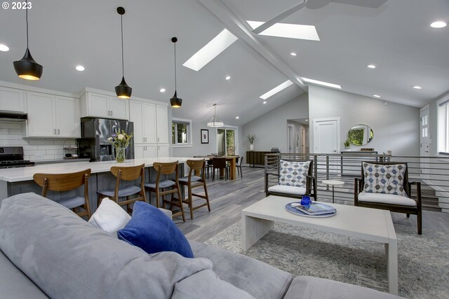 living room with a skylight, light hardwood / wood-style floors, high vaulted ceiling, and beamed ceiling