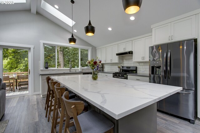 kitchen featuring pendant lighting, light stone counters, a skylight, backsplash, and stainless steel appliances