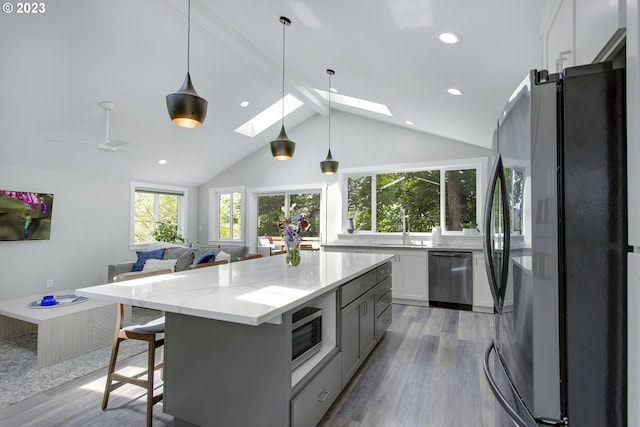 kitchen featuring a skylight, beamed ceiling, stainless steel appliances, light stone countertops, and white cabinetry