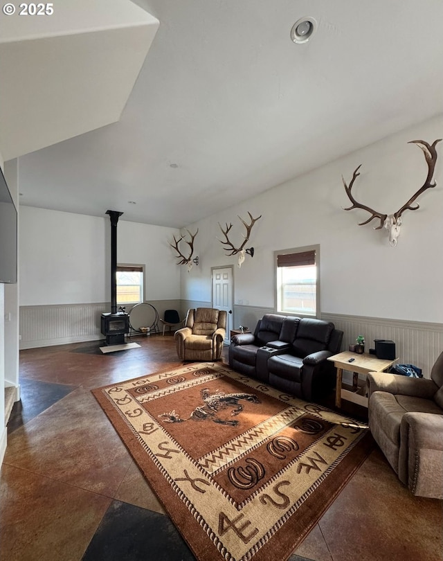 living area featuring a wealth of natural light, a wainscoted wall, a wood stove, and lofted ceiling