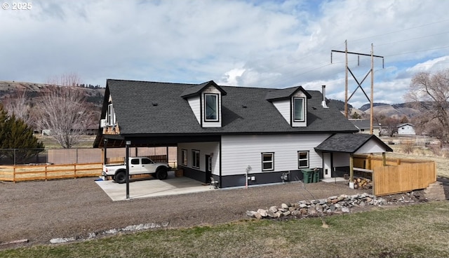 rear view of house featuring a carport, driveway, roof with shingles, and fence