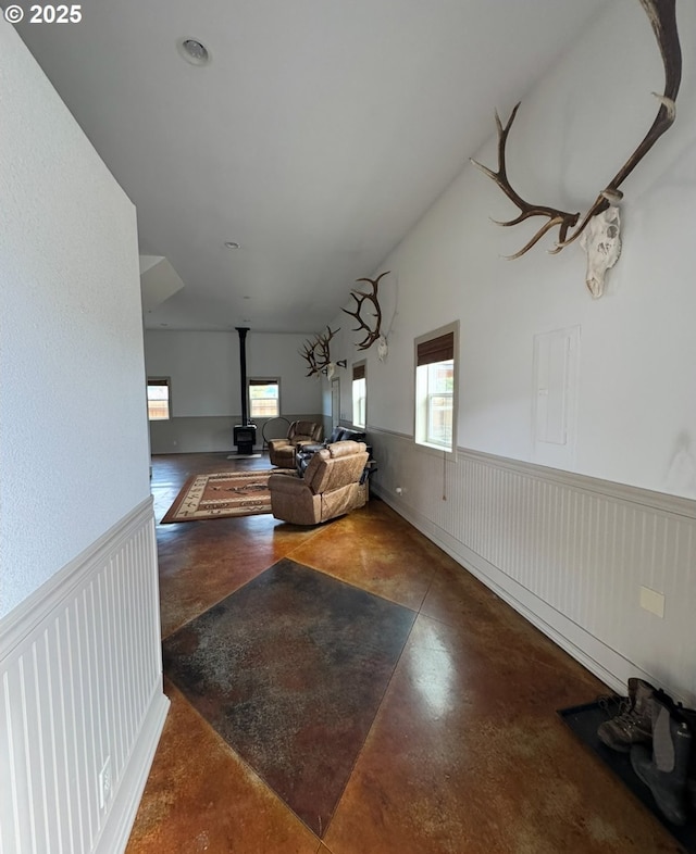 living area featuring electric panel, concrete flooring, wainscoting, and a wood stove