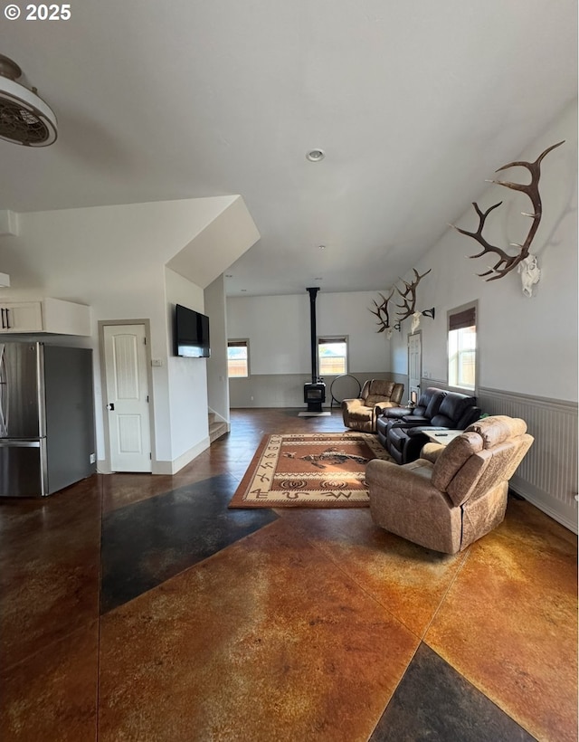 living area featuring a wainscoted wall, concrete flooring, and a wood stove