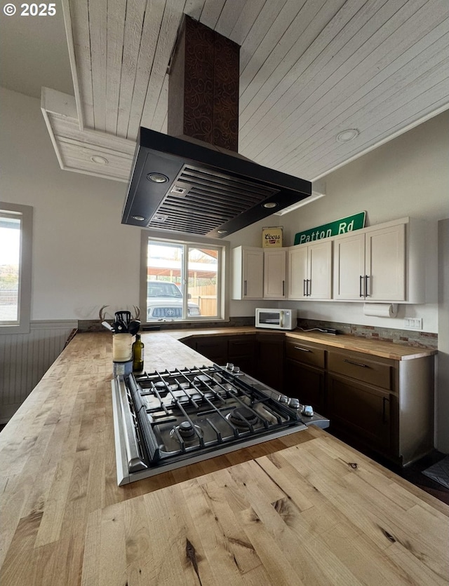 kitchen featuring white microwave, cooktop, island exhaust hood, white cabinets, and wood counters