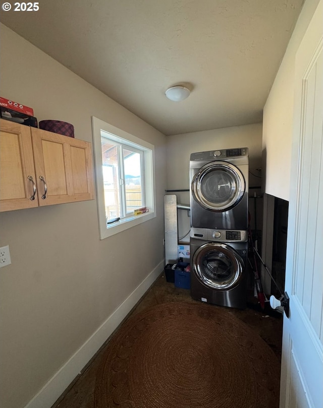 clothes washing area with stacked washer and dryer, cabinet space, and baseboards