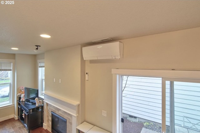 living room featuring plenty of natural light, wood finished floors, a fireplace, and a wall mounted AC