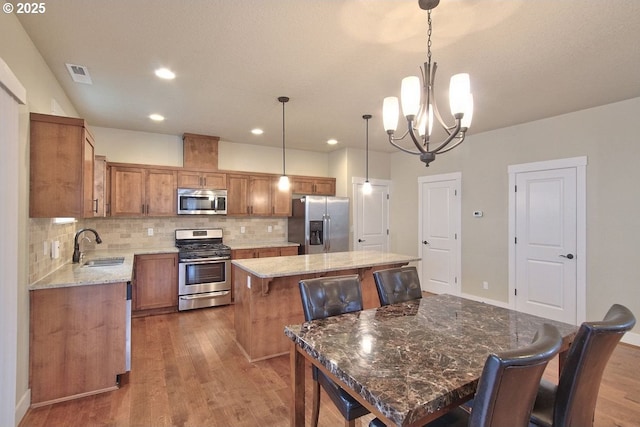 kitchen featuring wood finished floors, visible vents, a kitchen island, a sink, and stainless steel appliances