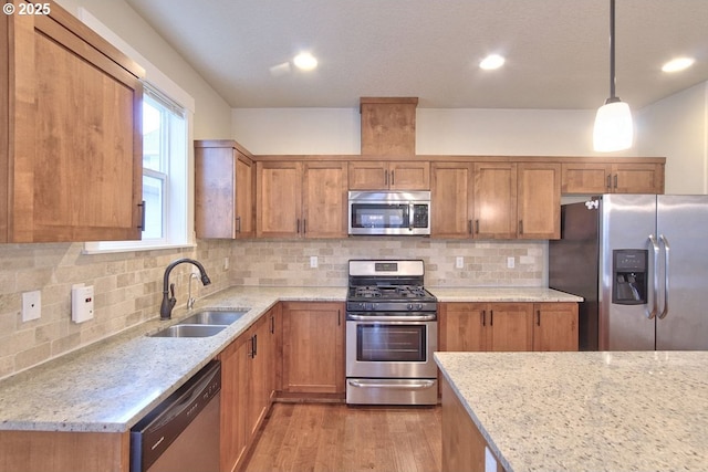 kitchen featuring light stone counters, brown cabinetry, appliances with stainless steel finishes, and a sink