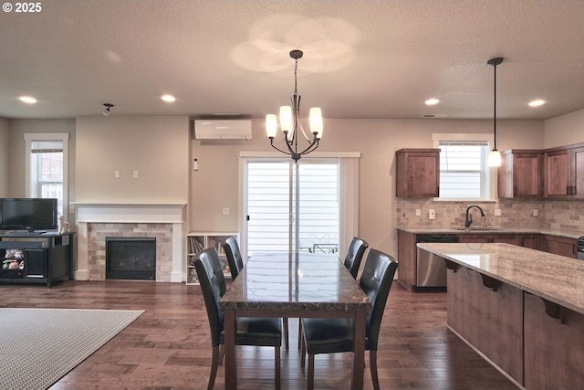 dining space featuring an AC wall unit, a notable chandelier, a fireplace, and dark wood-style flooring