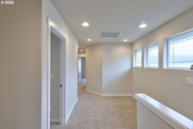 hallway with visible vents, a textured ceiling, recessed lighting, baseboards, and light colored carpet