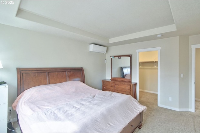 bedroom with a walk in closet, baseboards, an AC wall unit, light carpet, and a raised ceiling