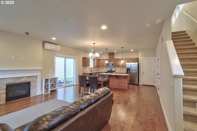 living area with stairs, a wall unit AC, a notable chandelier, and dark wood-style flooring