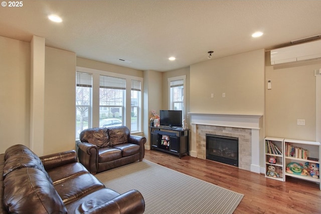 living area with wood finished floors, visible vents, a wall mounted AC, recessed lighting, and a glass covered fireplace