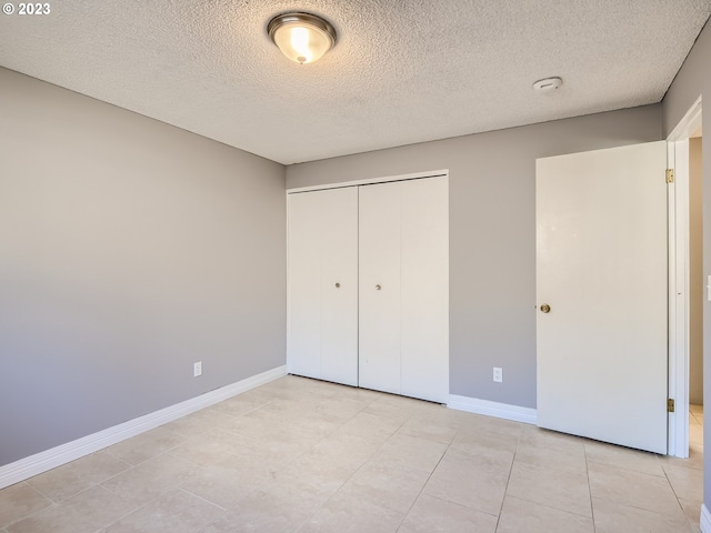 unfurnished bedroom with a textured ceiling, a closet, and light tile floors