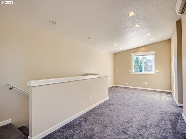 carpeted empty room with a wall mounted air conditioner, vaulted ceiling, and a textured ceiling