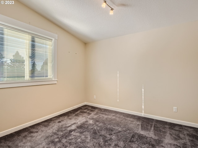 empty room with dark carpet, vaulted ceiling, a textured ceiling, and track lighting