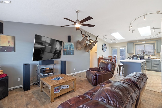 living room featuring hardwood / wood-style flooring, french doors, ceiling fan, and lofted ceiling with skylight