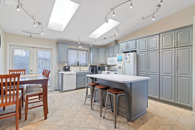 kitchen featuring sink, white appliances, light tile patterned flooring, a kitchen island, and lofted ceiling with skylight