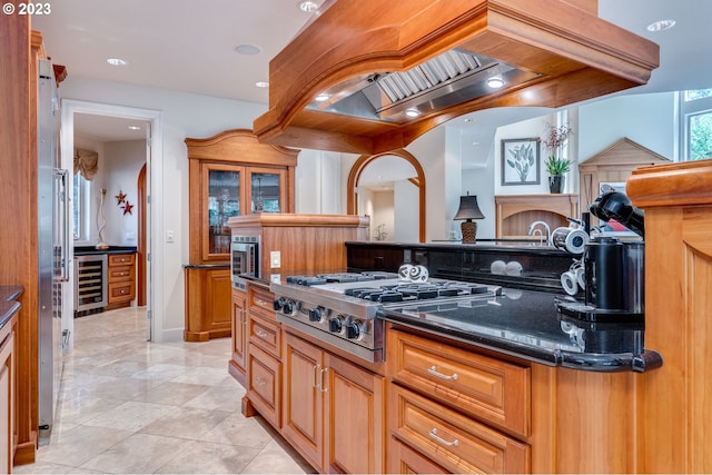 kitchen with light tile flooring, custom exhaust hood, stainless steel appliances, beverage cooler, and dark stone counters