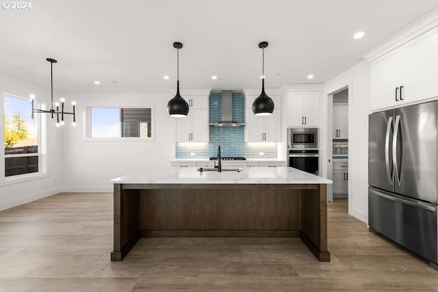 kitchen featuring a kitchen island with sink, appliances with stainless steel finishes, white cabinets, and wall chimney range hood