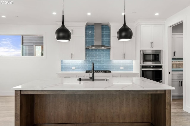 kitchen featuring wall chimney range hood, appliances with stainless steel finishes, white cabinets, and decorative light fixtures