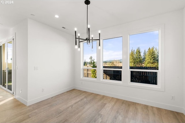 unfurnished dining area with plenty of natural light, a notable chandelier, and light hardwood / wood-style flooring