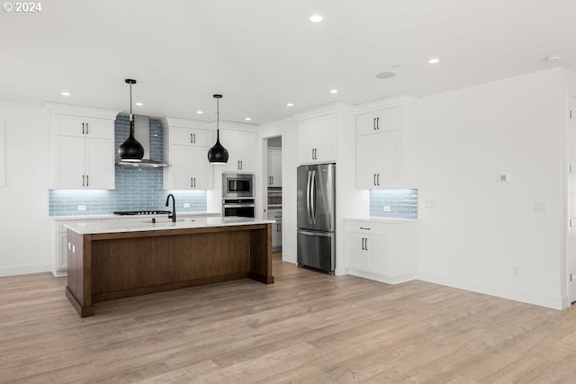 kitchen featuring light wood-type flooring, appliances with stainless steel finishes, an island with sink, and wall chimney range hood