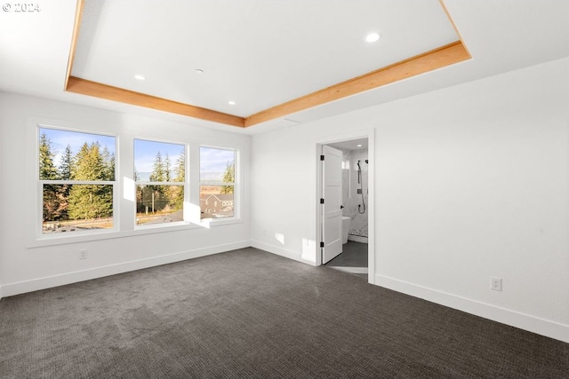 unfurnished bedroom featuring dark carpet, connected bathroom, and a raised ceiling