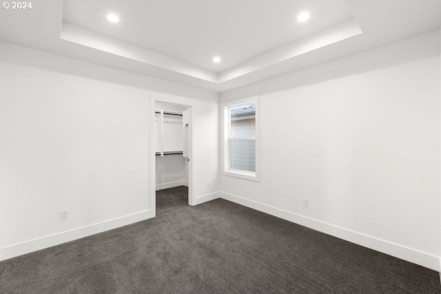 unfurnished bedroom featuring a tray ceiling, dark carpet, a walk in closet, and a closet