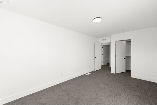 unfurnished bedroom featuring a walk in closet, dark colored carpet, and a closet