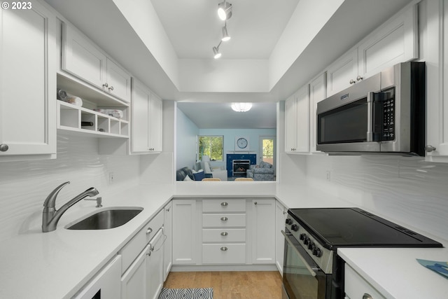 kitchen featuring high end black range oven, sink, rail lighting, white cabinets, and light hardwood / wood-style flooring