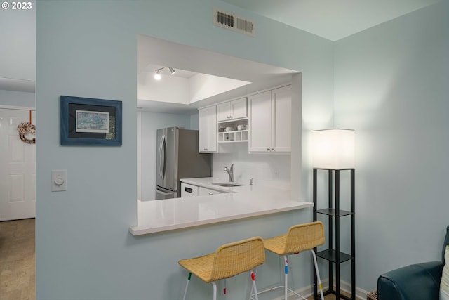 kitchen with a breakfast bar area, white cabinetry, kitchen peninsula, stainless steel fridge, and sink