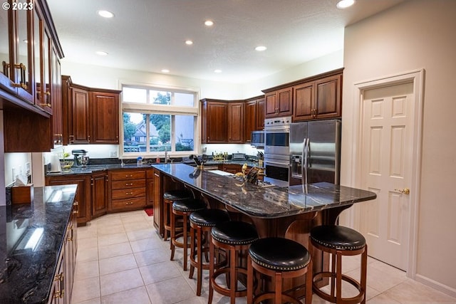 kitchen with appliances with stainless steel finishes, dark stone counters, a breakfast bar area, and a kitchen island with sink