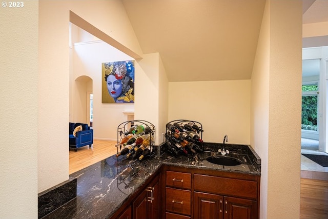 interior space featuring dark stone countertops, sink, light wood-type flooring, and vaulted ceiling